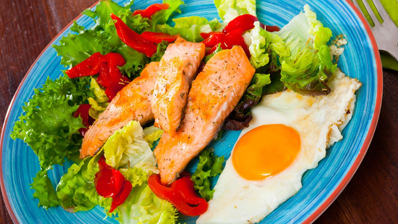 Low-calorie healthy breakfast with roasted trout, scrambled eggs and fresh vegetables