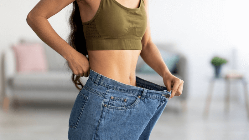 Successful weight loss diet concept. Cropped view of young Indian lady in big jeans demonstrating results of her slimming program, promoting healthy eating at home, closeup